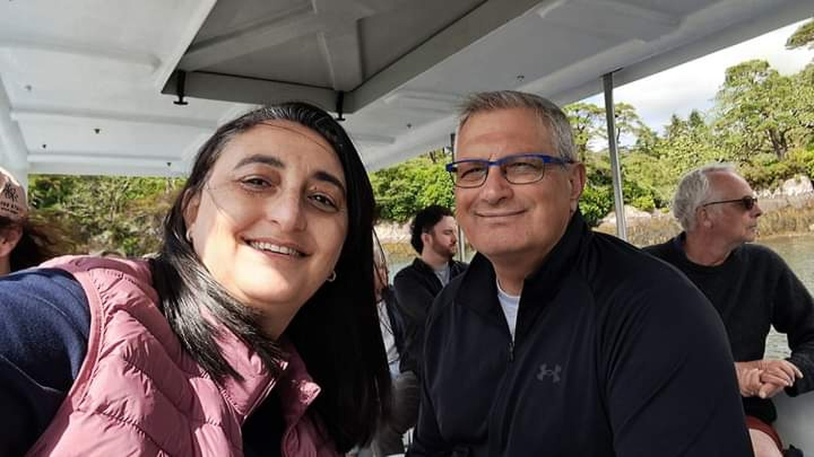 Albert and his wife Luisa smiling together on a lake boat, trees and water behind them
