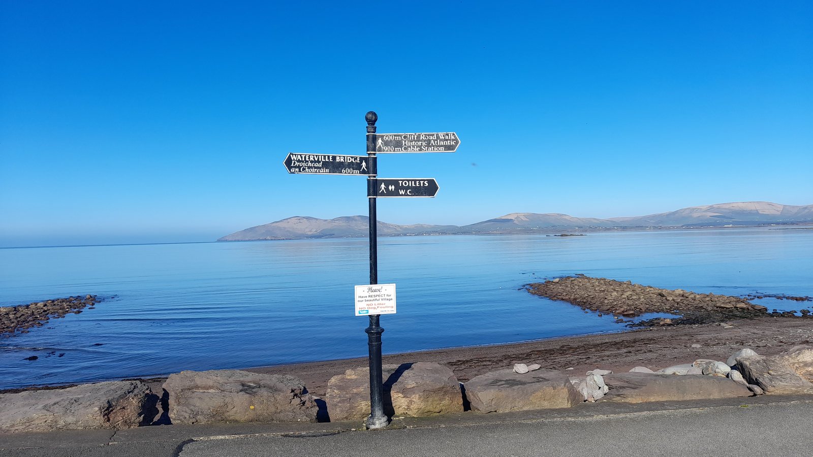 A black fingerpost at Waterville, County Kerry, pointing along the coast road under a clear blue sky